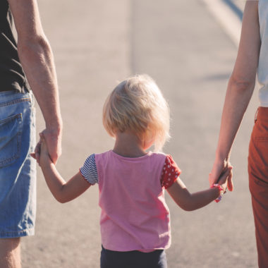 Small child holding hands with two adults while walking outdoors