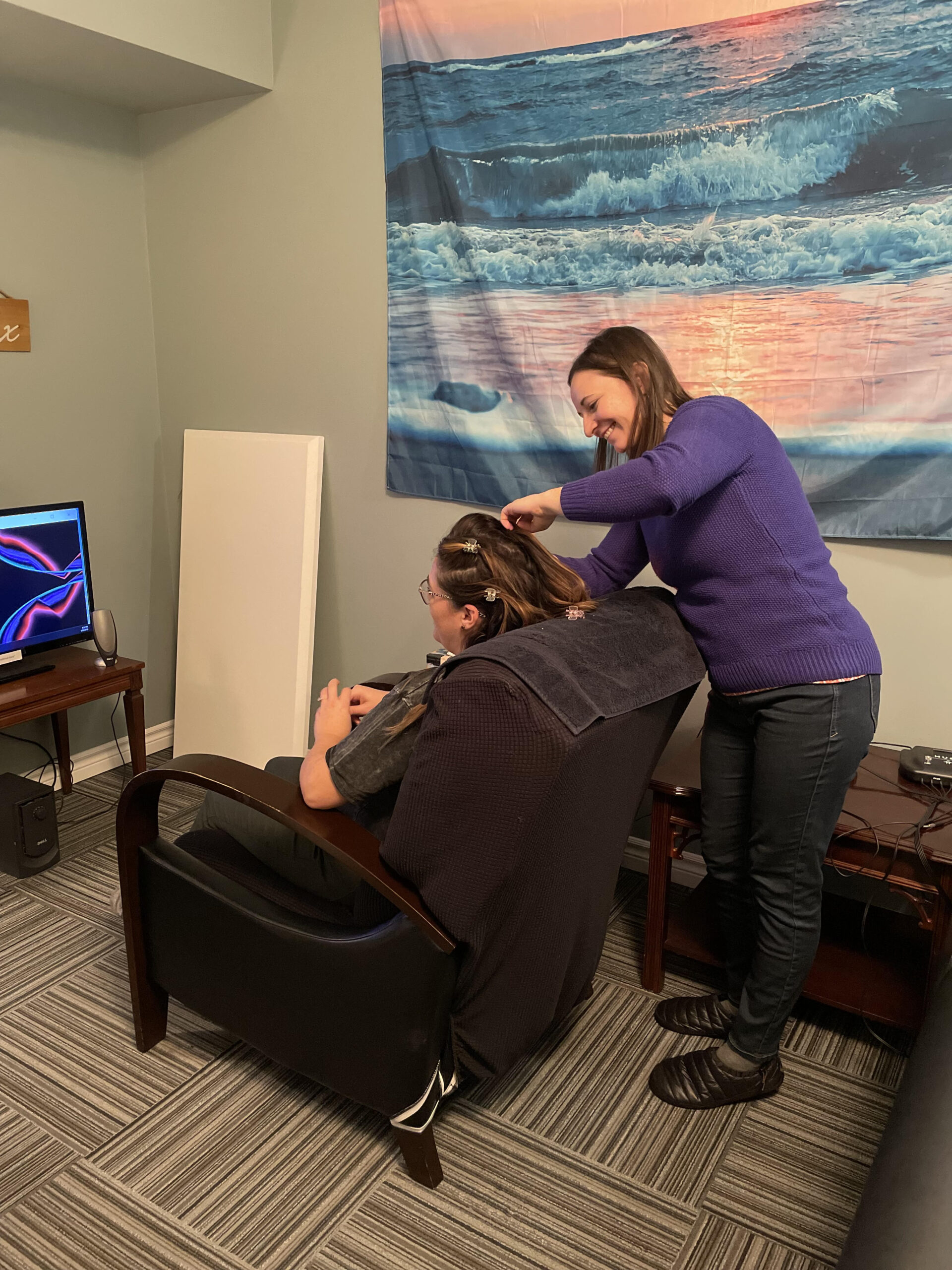 Practitioner placing neurofeedback sensors on a seated client in a calm treatment room
